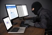 Hacker Wearing Balaclava Hacking Computers At Desk