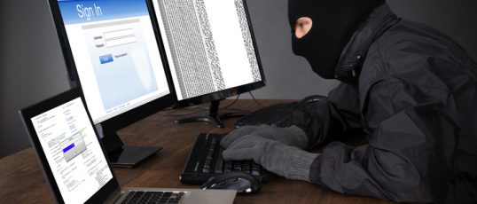 Hacker Wearing Balaclava Hacking Computers At Desk